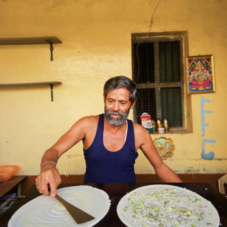 A cook spreading two dosas on a griddle