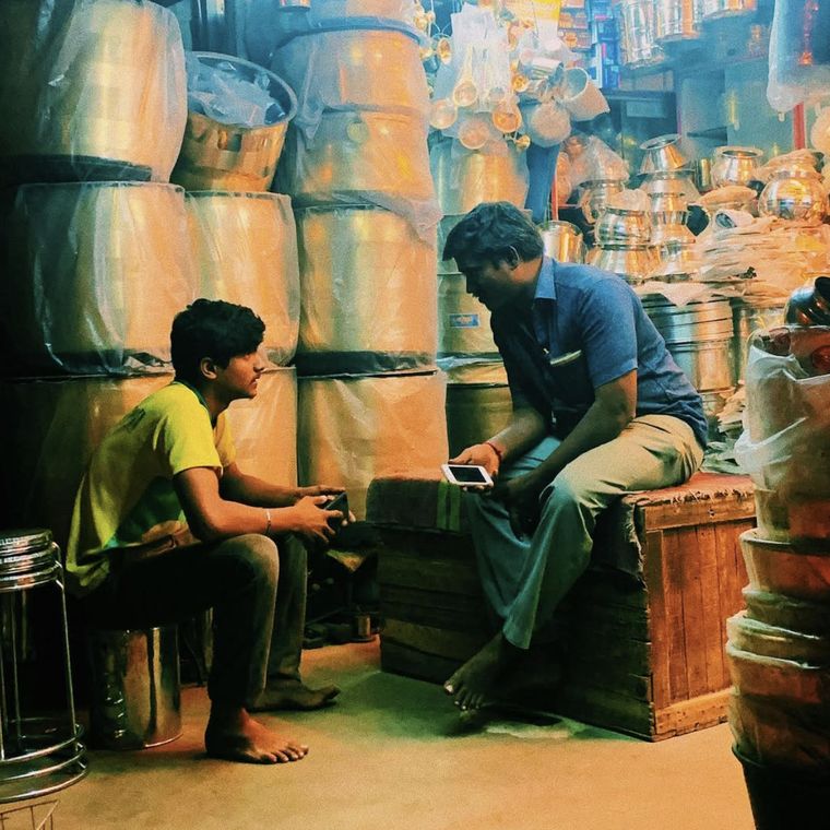 Two traders in a wholesale steel utensils shop, both looking at phones